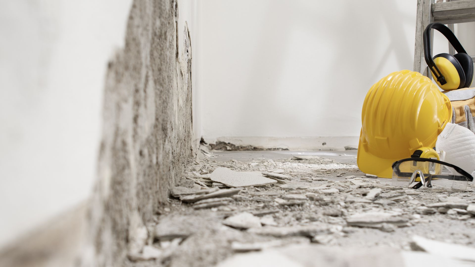 Construction worker in yellow hard hat inspecting debris in a damaged wall area