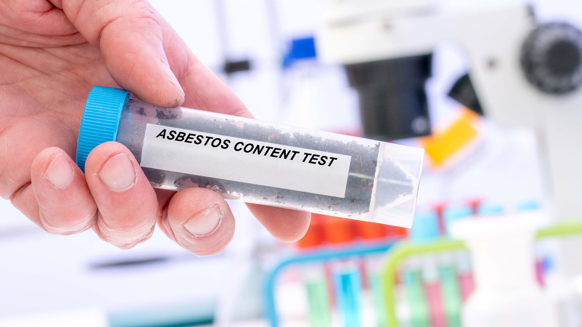 Hand holding a drug test vial labeled “SUBSTANCE CONTENT TEST” with lab equipment blurred in background