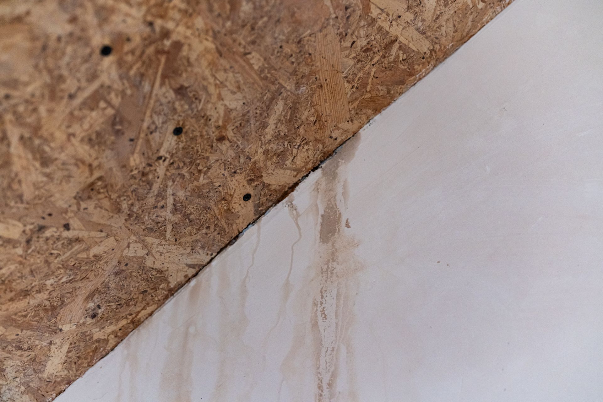 Water stain on a white wall beneath a plywood or wood panel edge