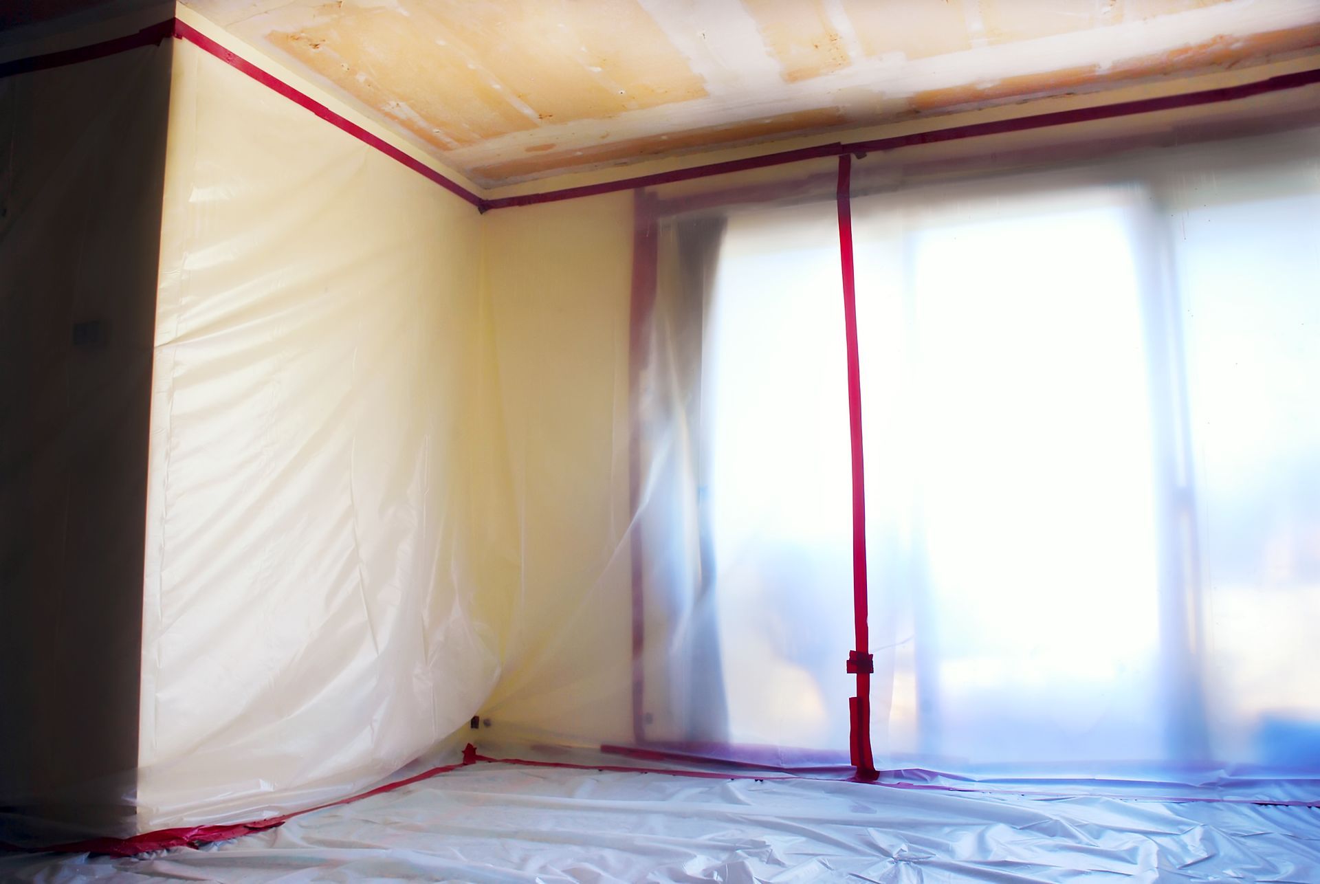 Empty room with white plastic sheeting and red tape along the ceiling and walls
