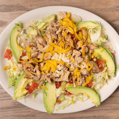 Plate of salad with lettuce, avocado slices, shredded cheese, and seasoned meat on a white dish