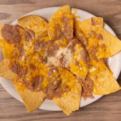 Plate of nachos topped with melted cheese and refried beans on a wooden table