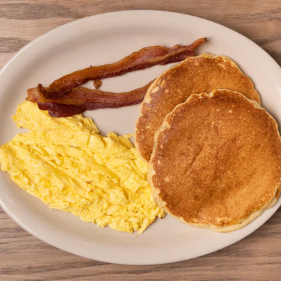 Scrambled eggs, two pancakes, and bacon on a white plate