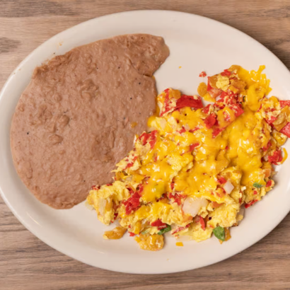 Scrambled eggs with red peppers and herbs beside a refried bean tortilla on a white plate