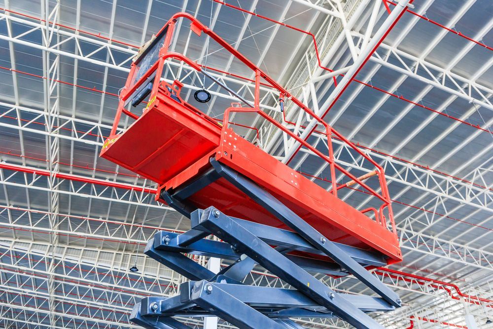 A Man Is Working On A Scissor Lift In Front Of A Large Building — B2B Hire In Garbutt, QLD