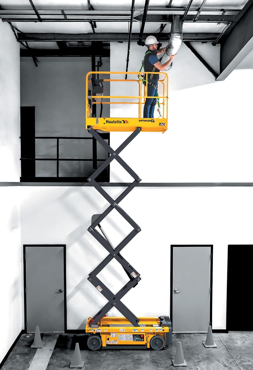A Man Is Standing On A Scissor Lift In A Room — B2B Hire In Garbutt, QLD