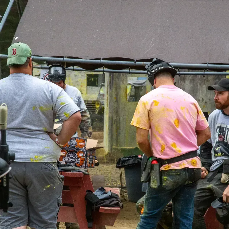 People in paintball gear at a paintball field. Some are covered in paint.