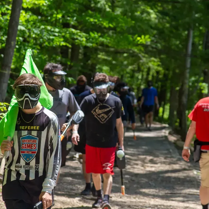 Group of paintball players walking through a forest path wearing masks and holding markers.