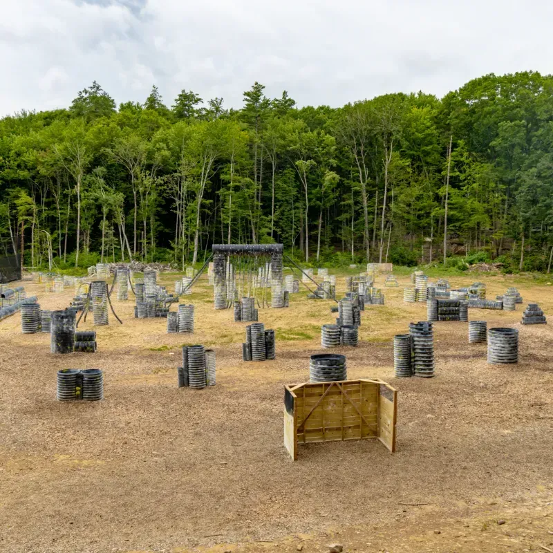 Paintball field with various obstacles, trees in the background, cloudy sky.