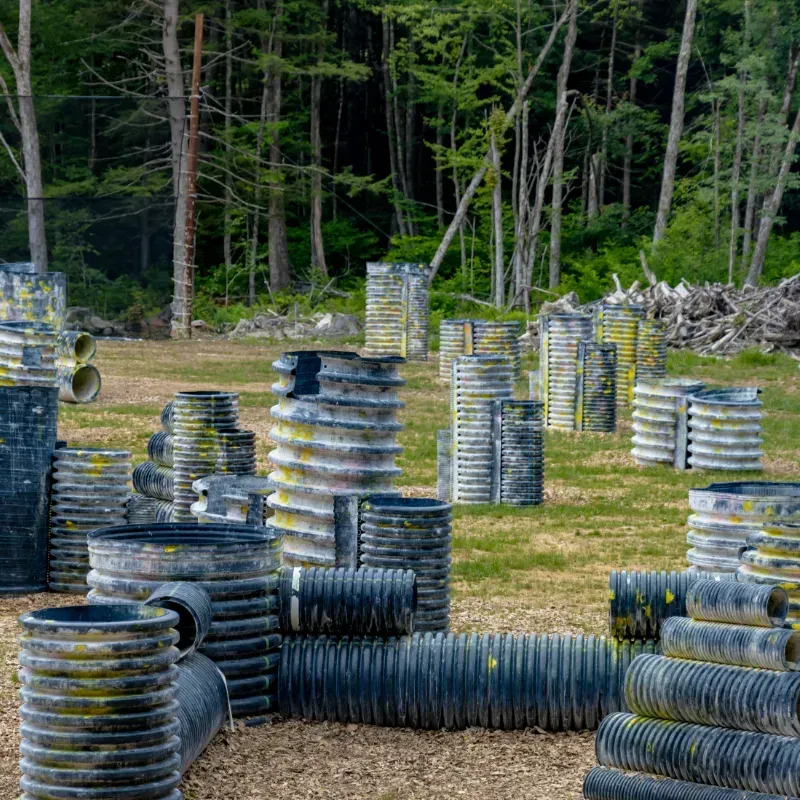 Paintball field with cylindrical bunkers, trees in the background, and grass ground.