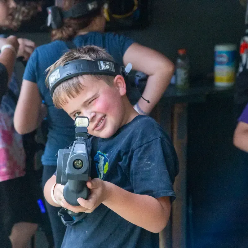 Boy winks while holding a laser tag gun, smiling. Indoors.