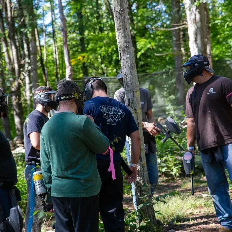 People playing paintball in a wooded area. Players wear protective gear and hold paintball guns.
