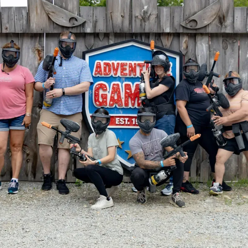 Group of people wearing paintball gear posing in front of Adventure Games sign.