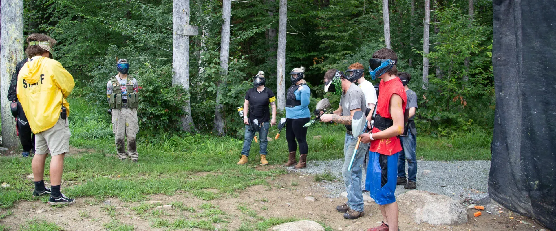 People wearing paintball masks and gear standing in a wooded area.
