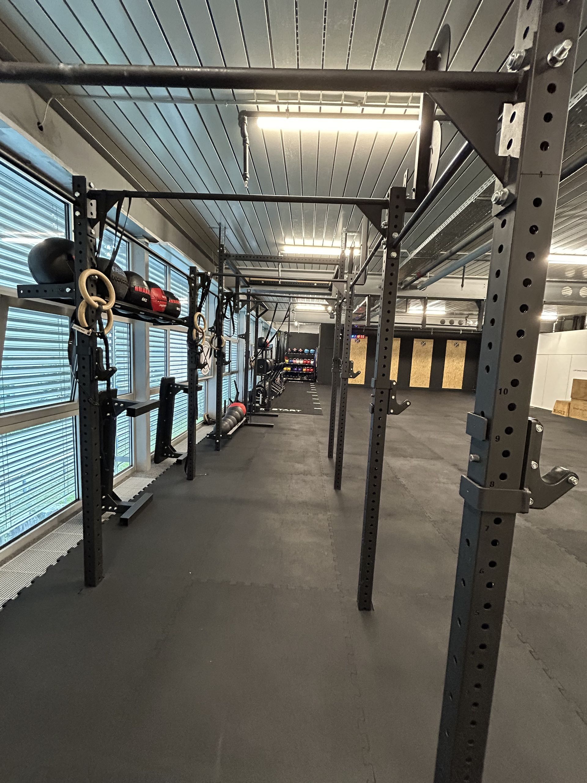 An indoor gym featuring a large metal pull-up and squat rig system with black rubber flooring and windows on the left.