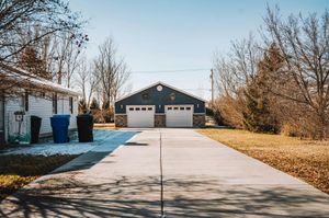 A concrete driveway leads toward a detached two-car garage with light blue siding under a bright, clear sky.