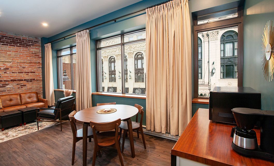 Cozy café interior with brick walls, teal accents, round table, chairs, curtains, and coffee machine on counter