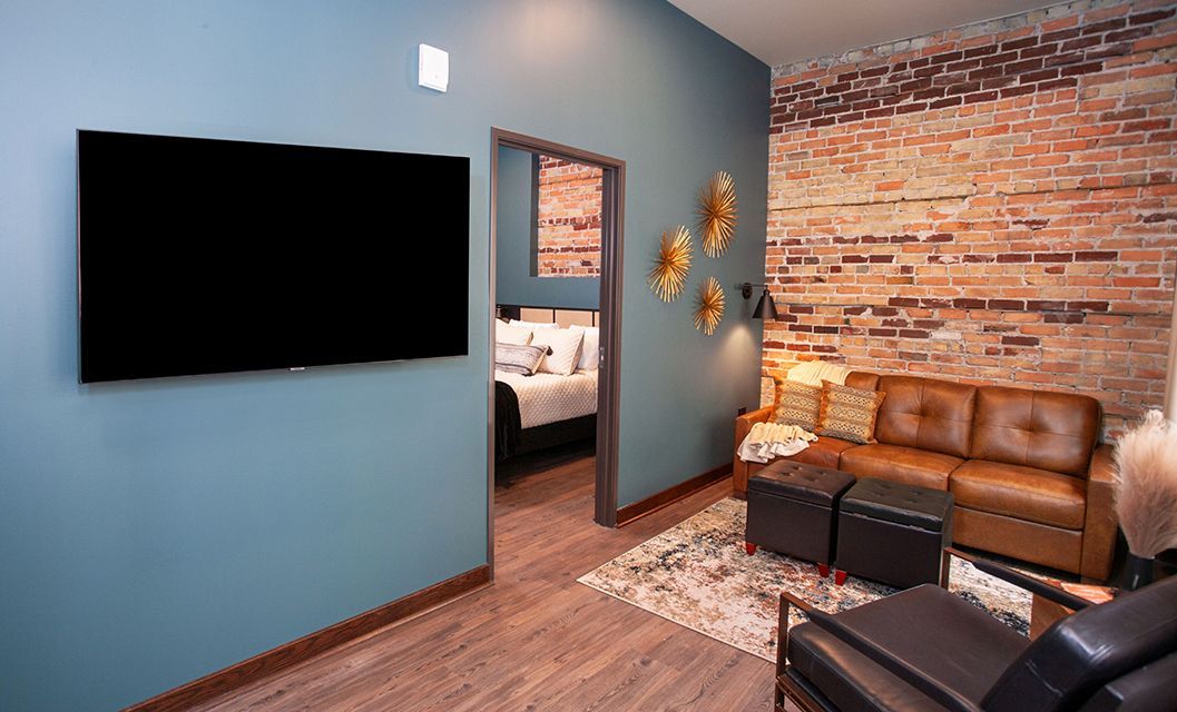 Modern living room with blue walls, brick accent wall, wall-mounted TV, and brown leather sofa.
