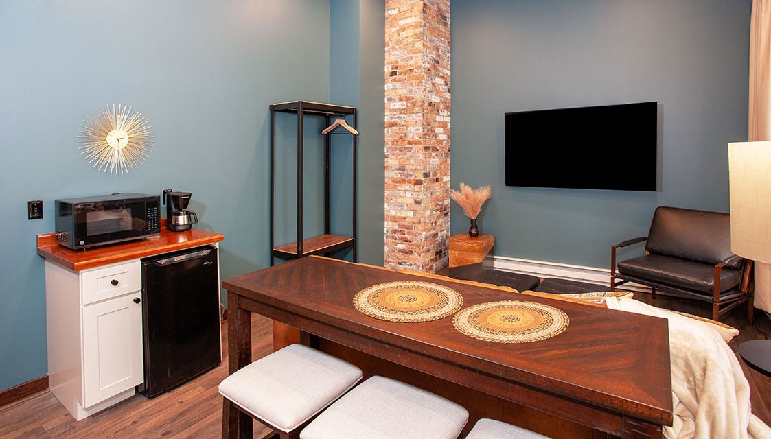 Modern dining area with wooden table, wall-mounted TV, brick column, and small wet bar area
