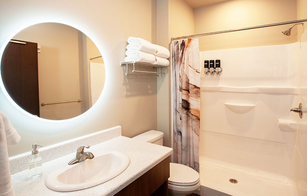 Bright bathroom with pedestal sink, round mirror, and walk-in shower with towels