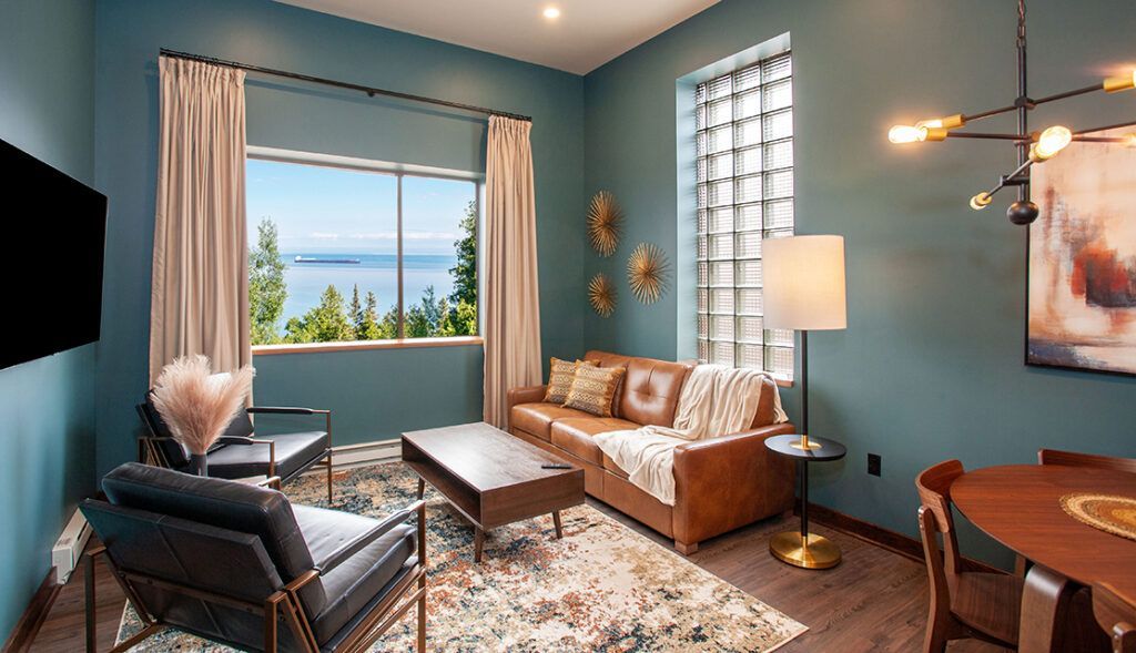 Modern living room with blue walls, leather sofa, armchair, coffee table, and a large window with curtains.