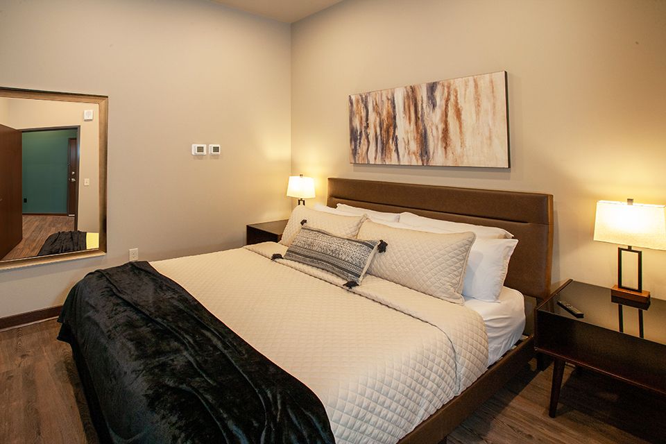 Cozy bedroom with a queen bed, bedside lamps, wall art, and a mirror on the left wall