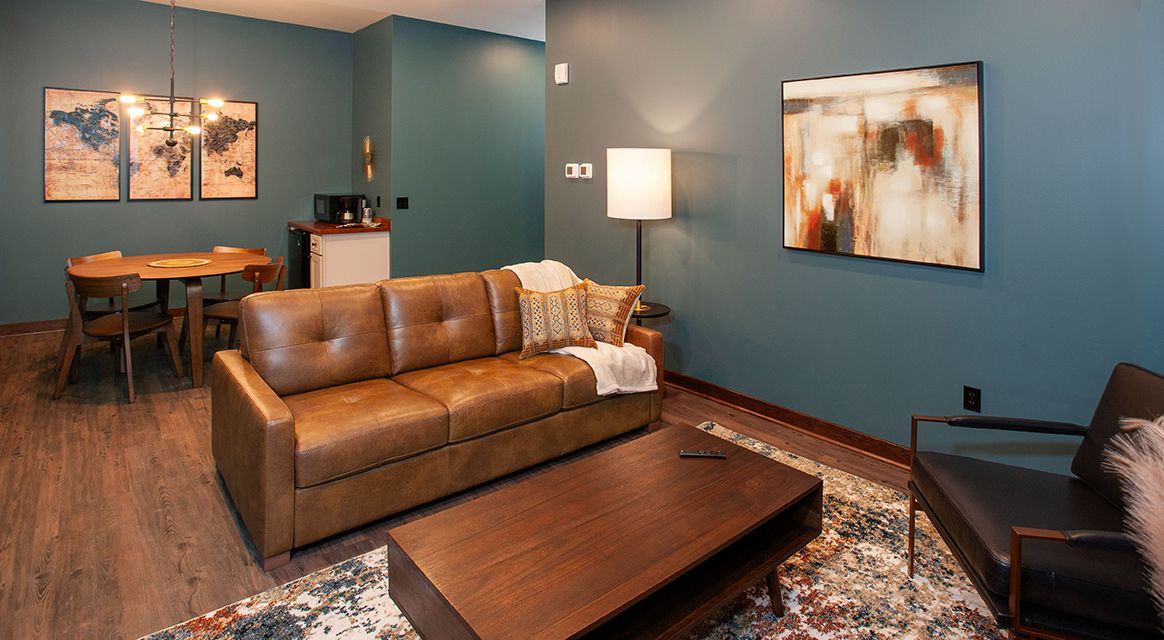 Modern living room with a brown leather sofa, coffee table, teal walls, lamp, and framed wall art.