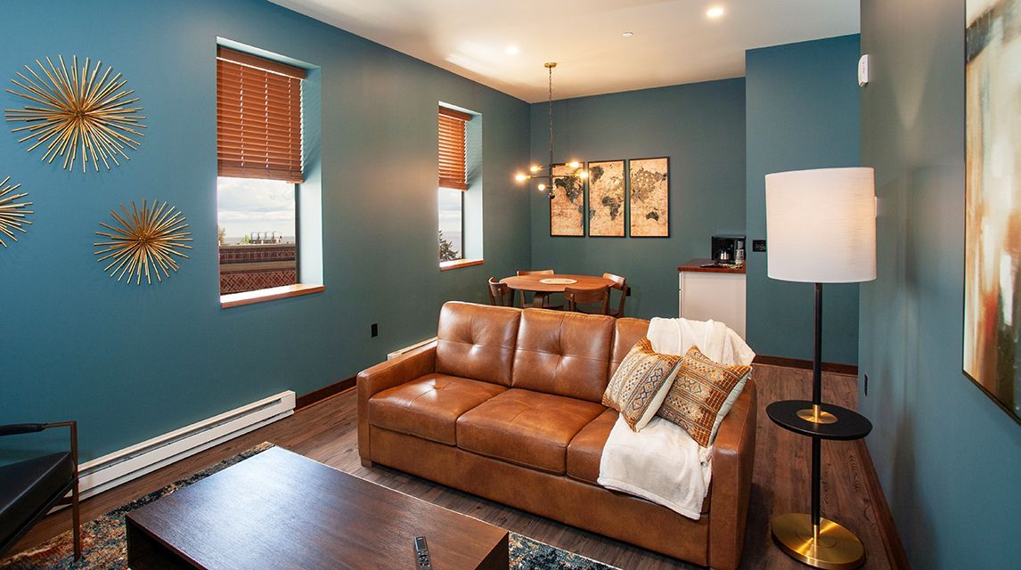 Cozy living room with teal walls, brown leather sofa, wood table, and floor lamp under warm lighting