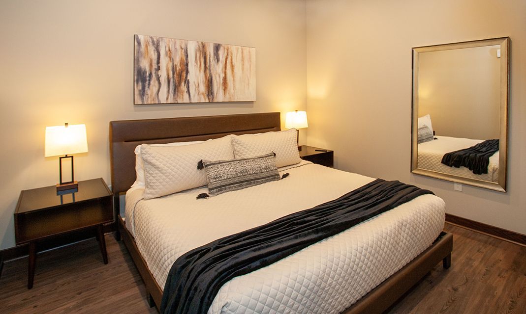 Modern bedroom with a king bed, bedside lamps, wall art, and a large mirror