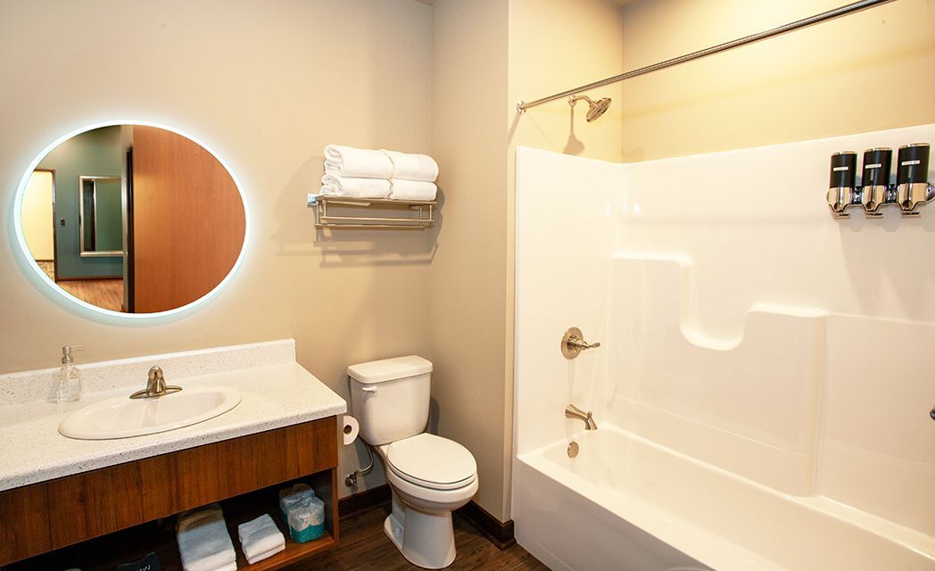 Modern bathroom with round mirror, white vanity, toilet, and shower tub