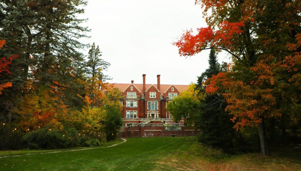A red-brick building beyond a green lawn, framed by autumn trees with red and orange leaves.