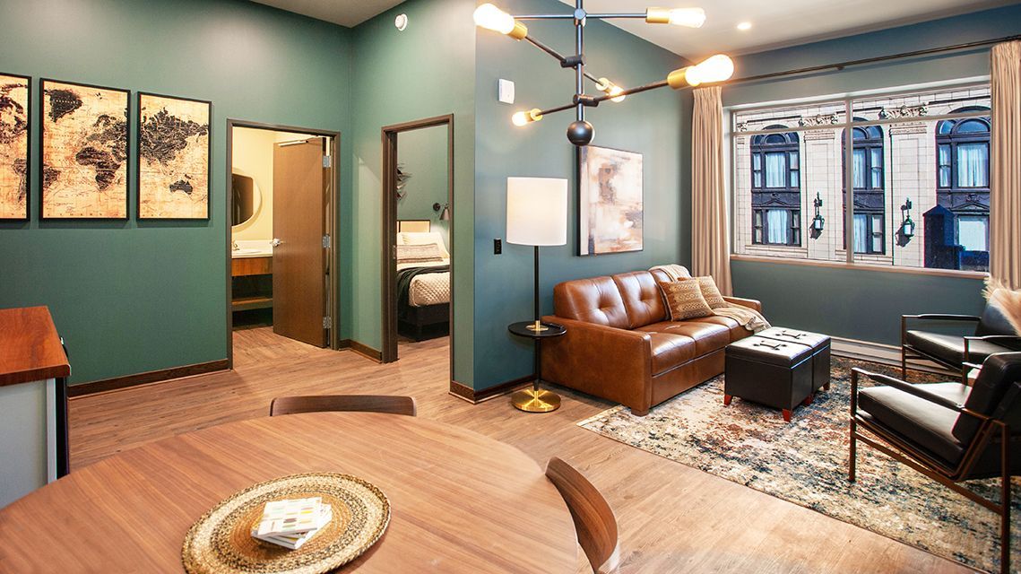 Stylish living room with teal walls, leather sofa, black chairs, large windows, and warm wood floors