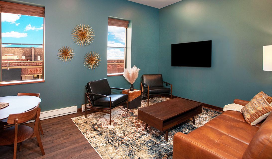 Modern living room with teal walls, leather chairs, wall-mounted TV, coffee table, and patterned rug