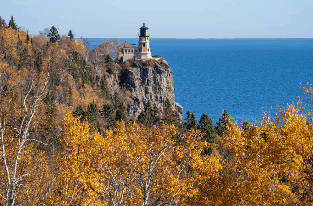 Lighthouse on a cliff above a blue lake, framed by autumn trees with golden foliage