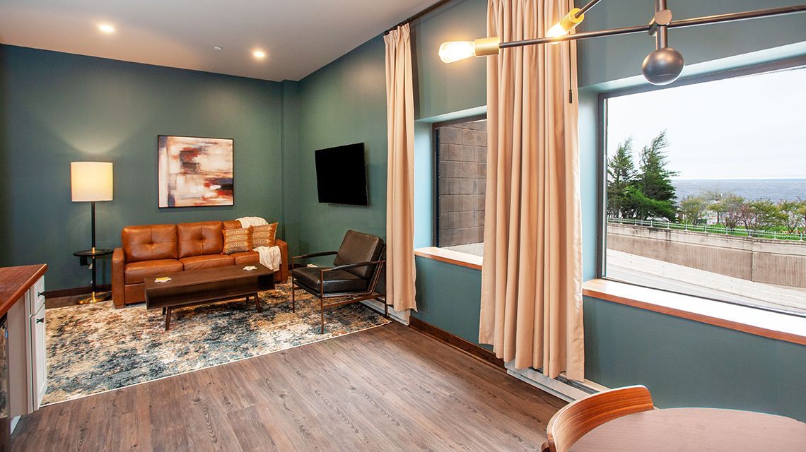 Modern living room with blue walls, tan sofa, patterned rug, and large window overlooking greenery