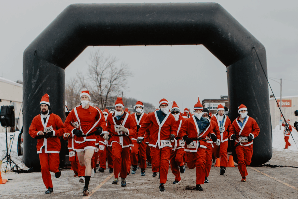 Santa-clad runners gather beneath a large black inflatable arch at a snowy start line.