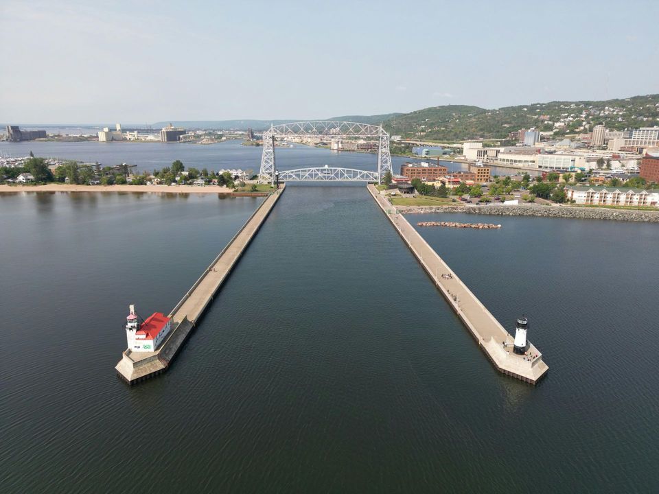 Aerial view of a long bridge over water leading to a harbor city with hills in the background.