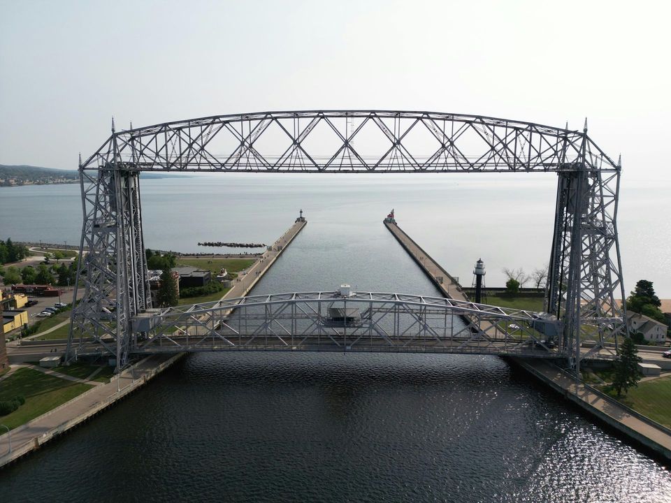 Steel lift bridge over calm water at a canal entrance, with open center span and hazy shoreline beyond