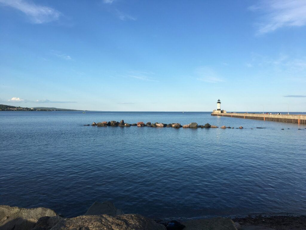 Calm blue harbor with a lighthouse on a breakwater under a clear sky