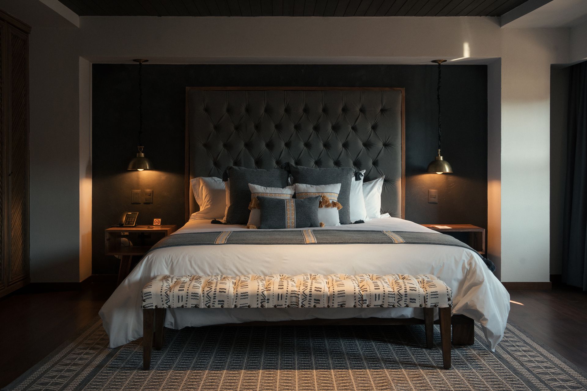 A bedroom with a bed , nightstands , lamps and a bench.