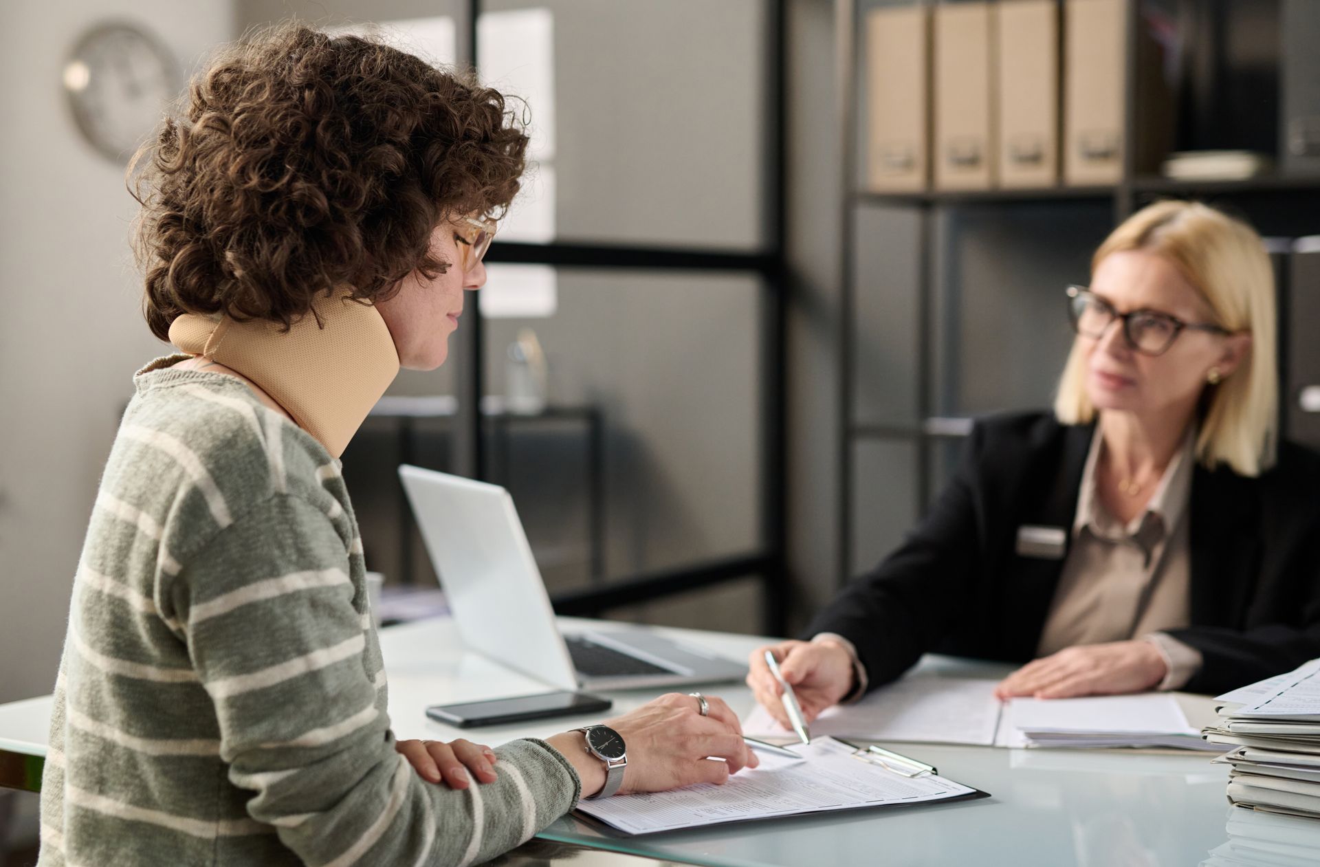 An injury lawyer meeting with a client wearing a neck brace to discuss a claim.
