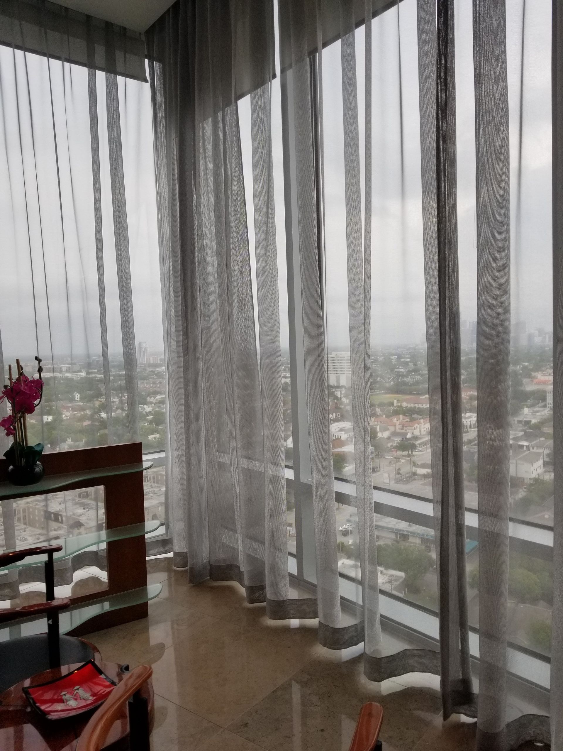 Sheer, striped grey curtains hang in front of large windows overlooking a city skyline.