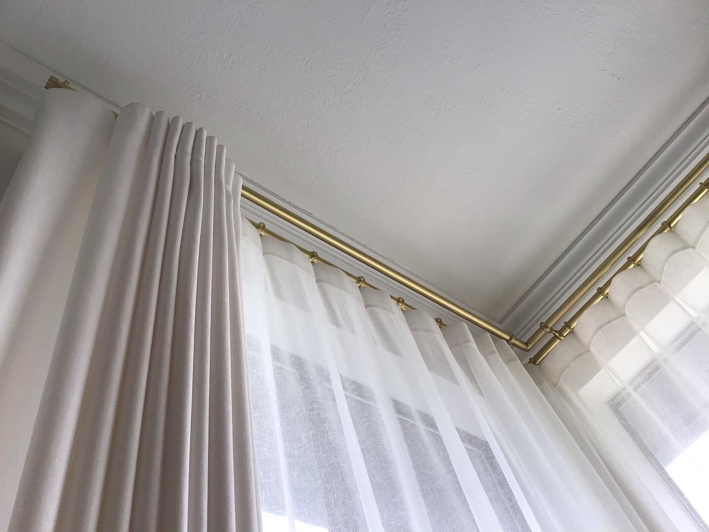 White floor-to-ceiling curtains hang from a gold track mounted to the ceiling in a corner.