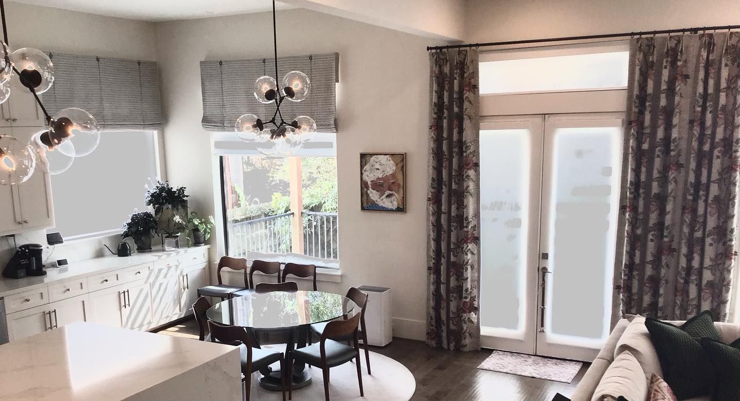 An open-concept room features a dining area with a round table, modern pendant lights, and floor-to-ceiling floral curtains.
