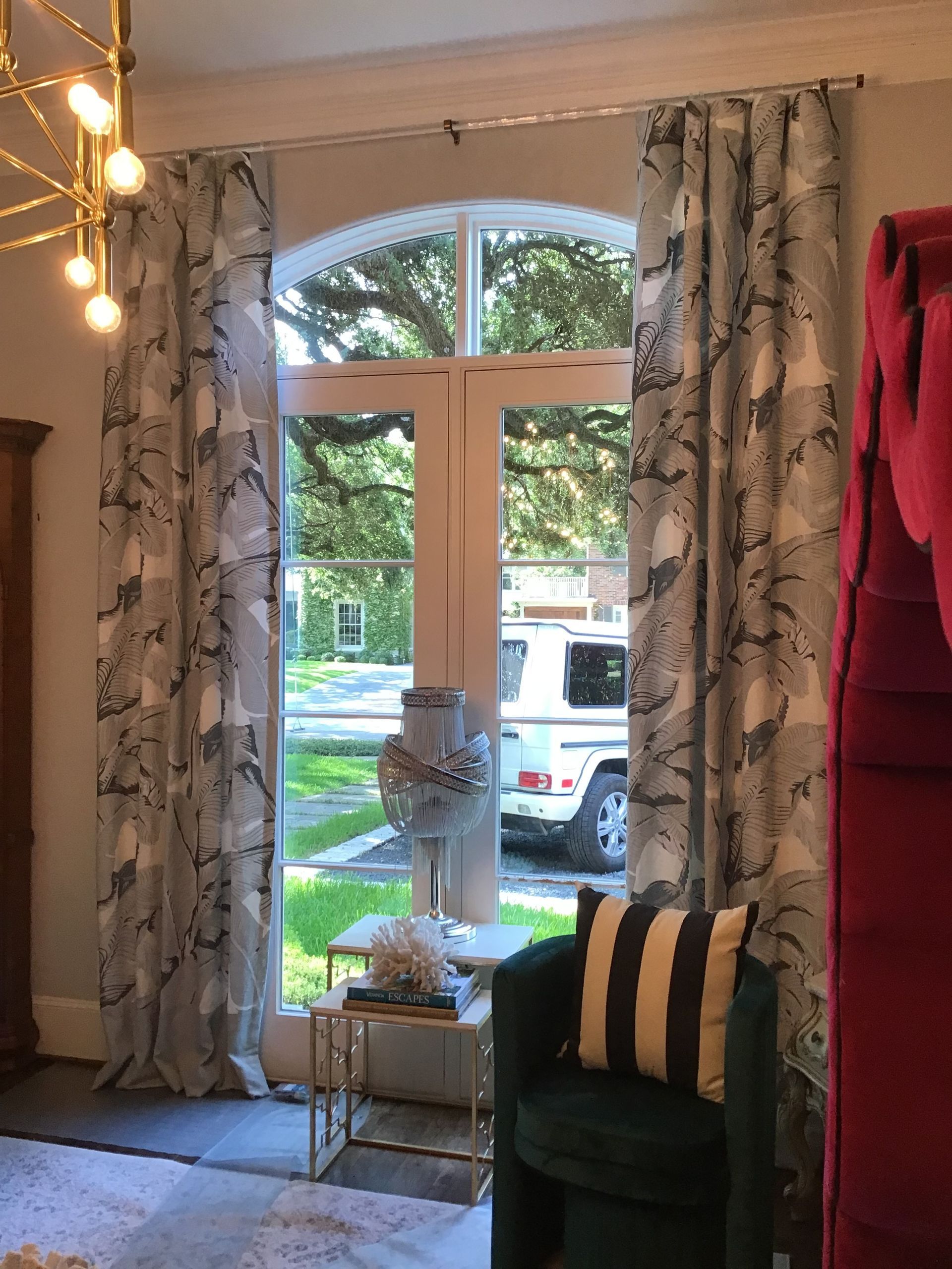 A window with patterned gray curtains, a side table with a lamp, and a green armchair with a striped pillow.