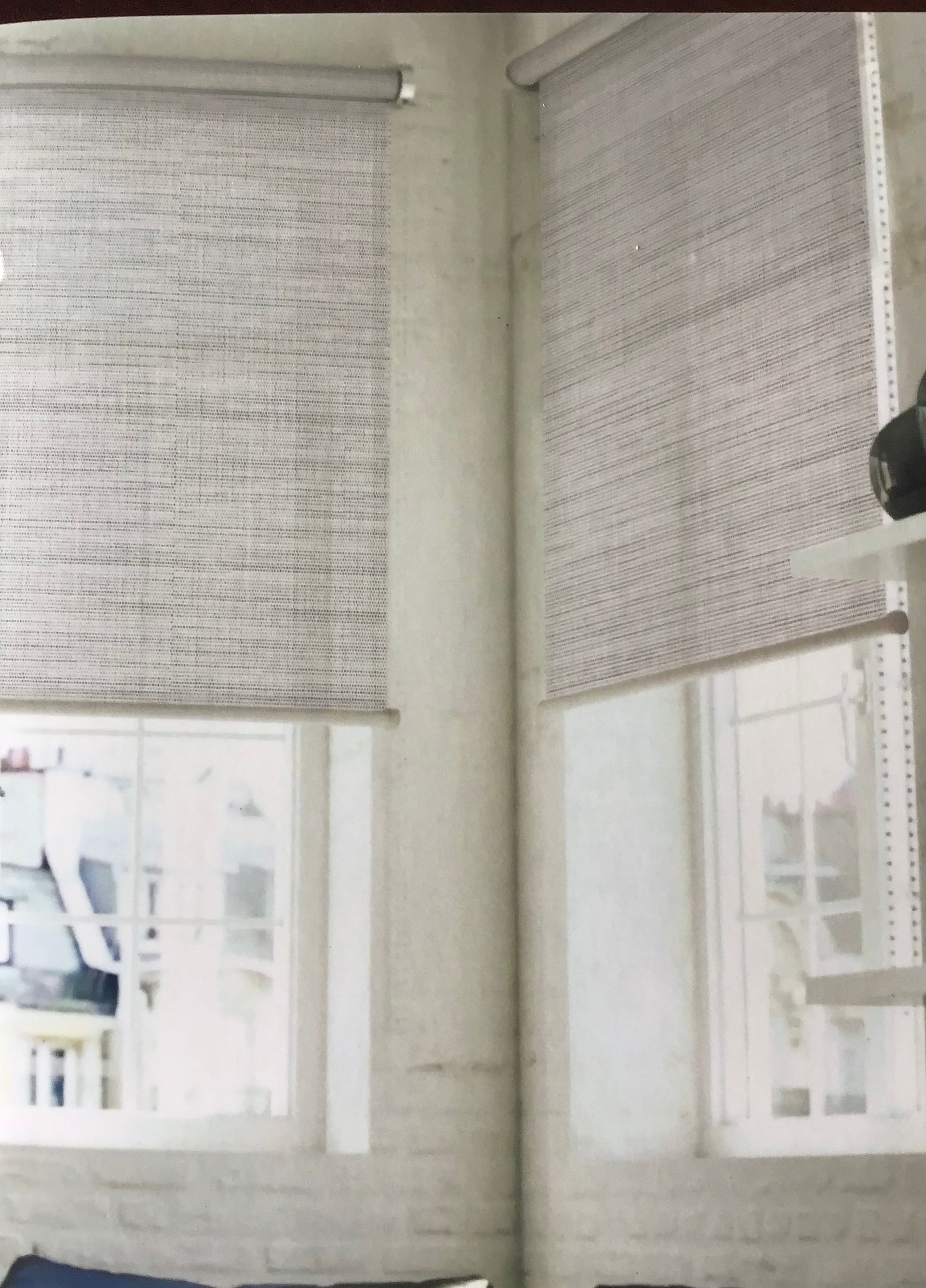 Two windows in a light-colored room with patterned roller shades featuring dark text or print on a cream background.