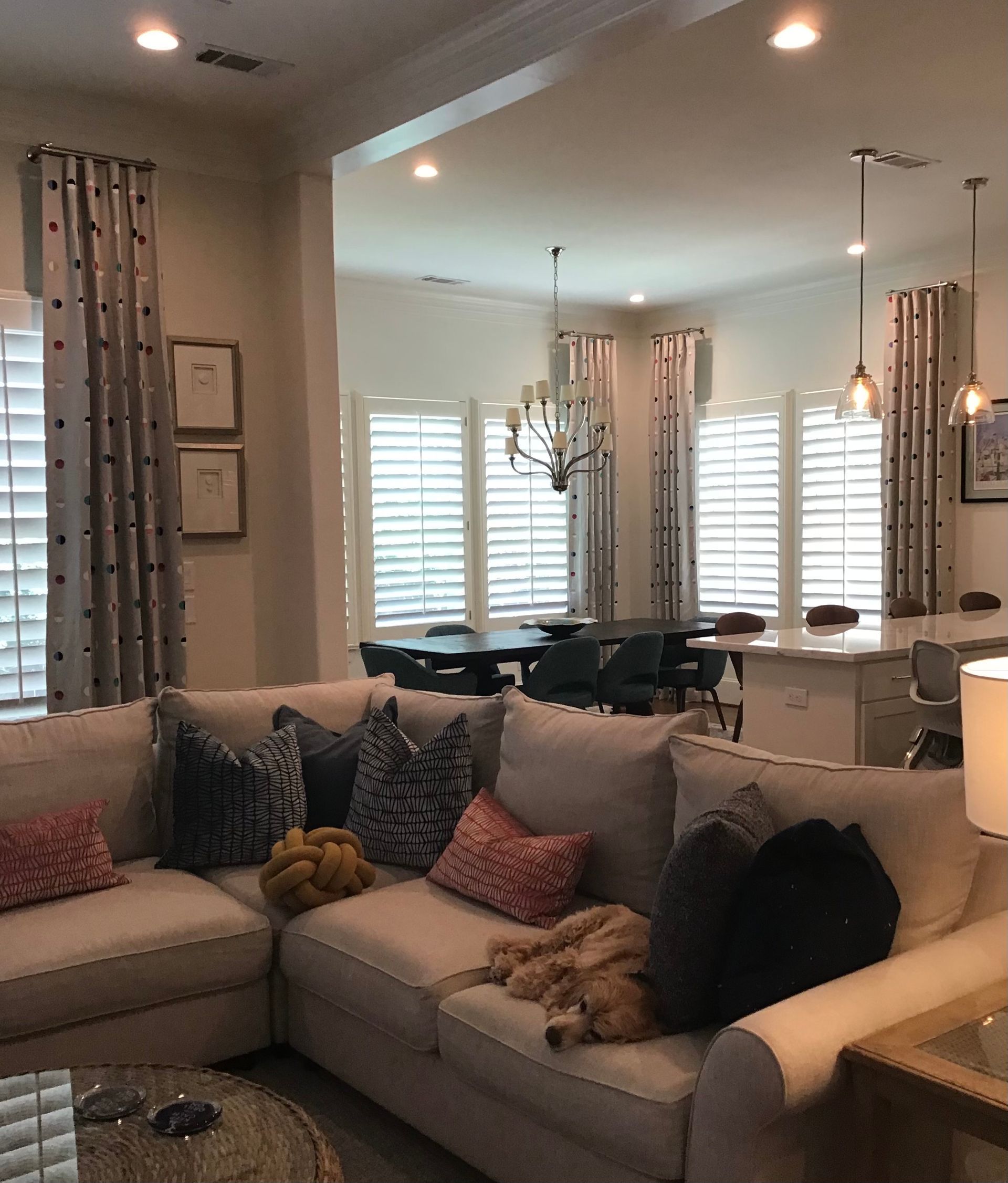 A beige sectional sofa with patterned pillows sits in a living room, featuring a golden retriever sleeping on the cushions.
