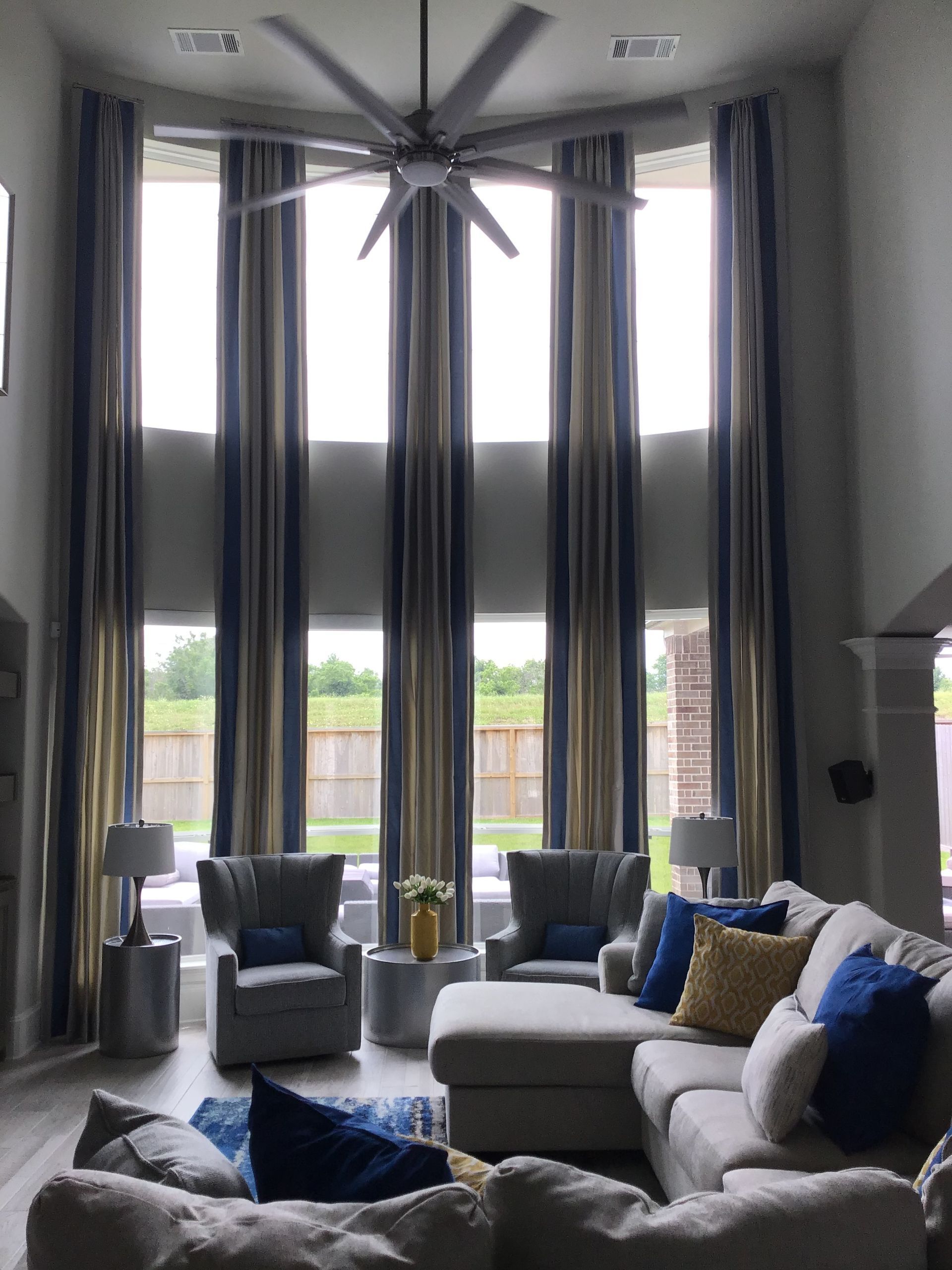 Tall living room with a sectional sofa and two armchairs facing floor-to-ceiling windows with striped drapes.