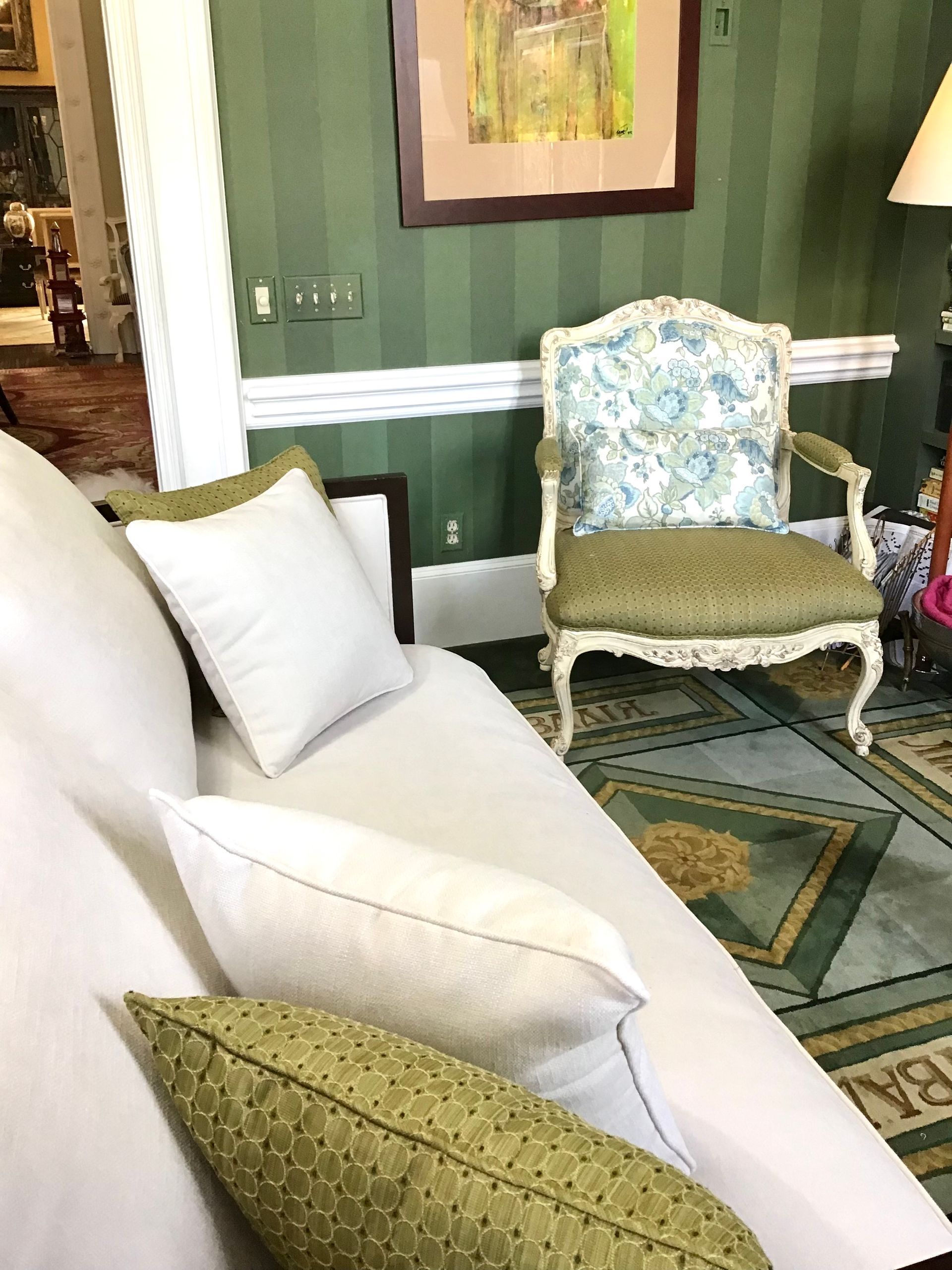 A white sofa with decorative throw pillows next to an ornate patterned armchair in a green-walled room.