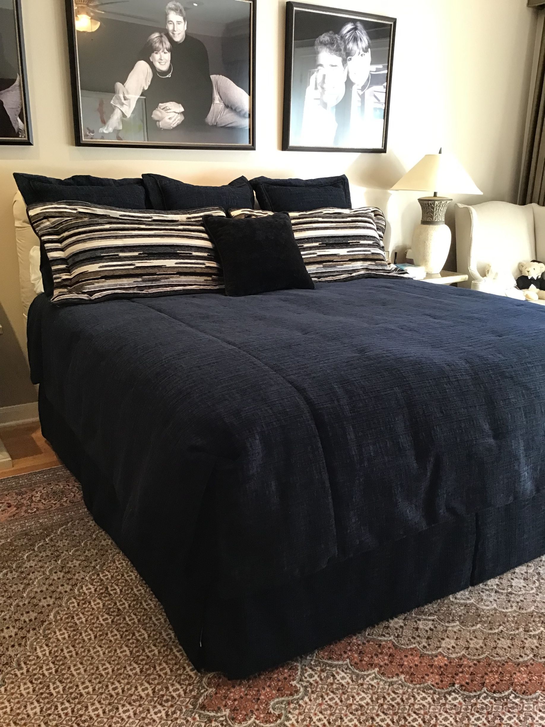 A bed with a dark blue comforter, striped pillows, and two framed photos on the wall in a bedroom with a patterned rug.